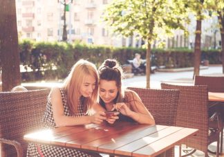 dua wanita sedang duduk sambil melihat smartphone